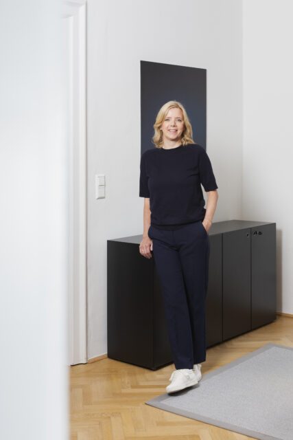 Smiling COX Coaching & Consulting employee in a bright office with a black shelf