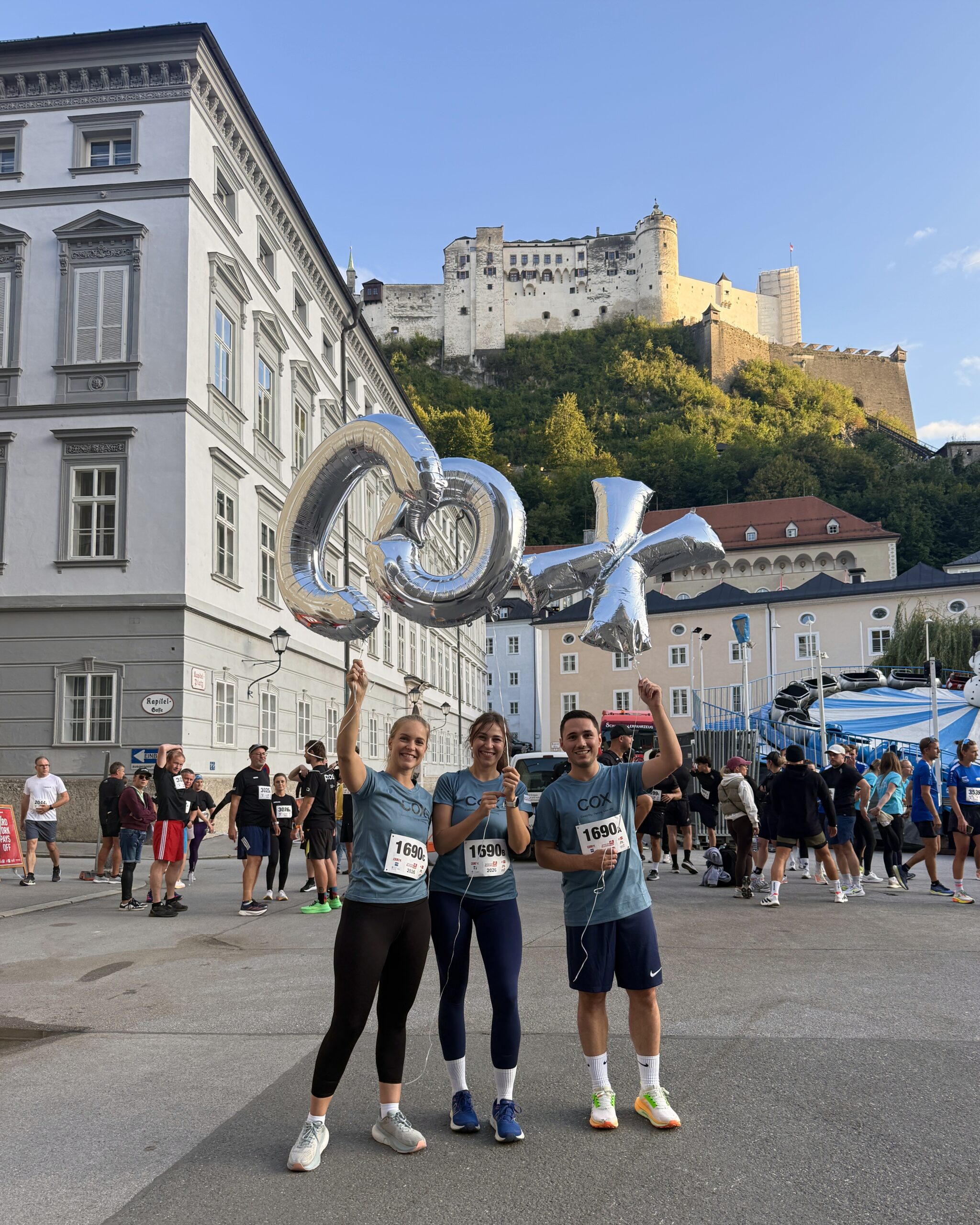 Drei COX Teammitglieder vor der Festung Hohensalzburg vor dem Start des Salzburger Businesslaufs 2026.